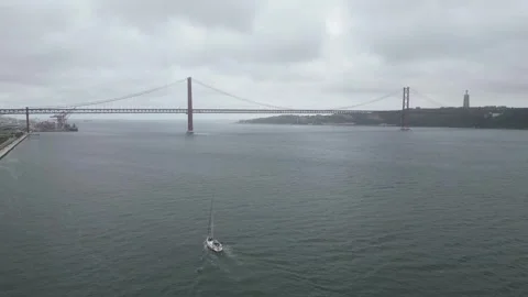 Lisbon's 25 de Abril Bridge with Sailing Boat on Cloudy Day Stock Footage 310614766