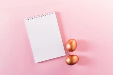 List or note book with set of golden eggs. Spring trendy composition on pastel Photos