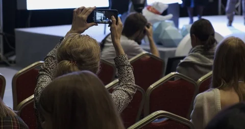 Listeners, hall presentations, viewers, back of head, woman takes on smartphone Stock Footage 126309115