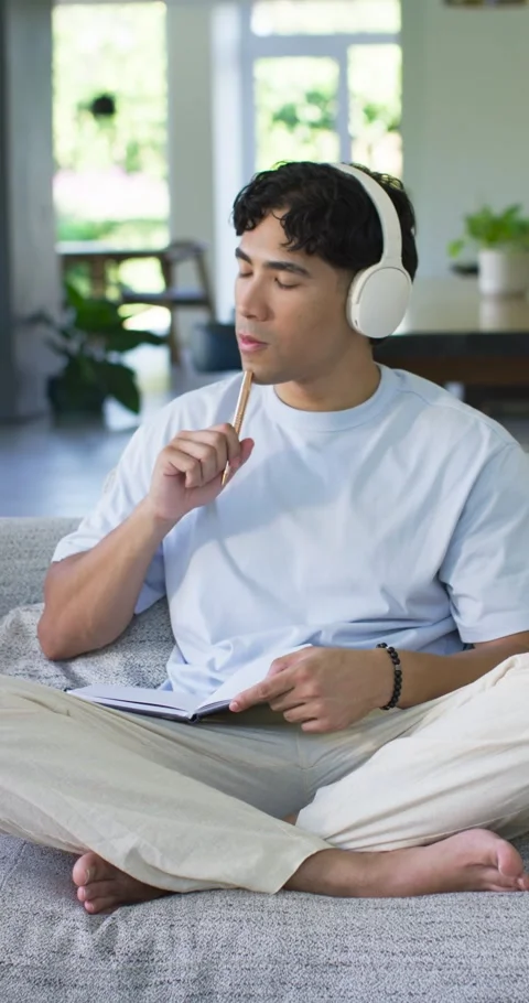 Listening man in light blue T-shirt tapping pencil, writing in notebook on couch Stock Footage 345493138