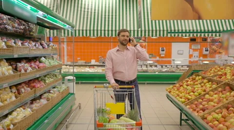 Listening to mobile phone while standing with basket in market Stock Footage 63377616
