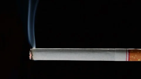 Lit and burning cigarette with smoke on black background . Vidéo 125541712