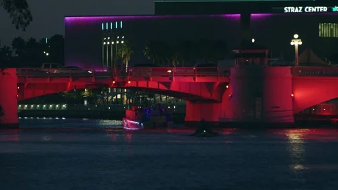 Lit up boats going under light covered bridge in Tampa Bay at night Stock Footage 113694192