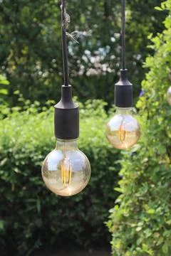 A lit bulb hanging with string lights in a garden setting Stock Photos