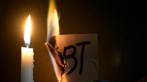 Lit candle burning a piece of paper with debt handwritten on it. Stock Footage 345914967