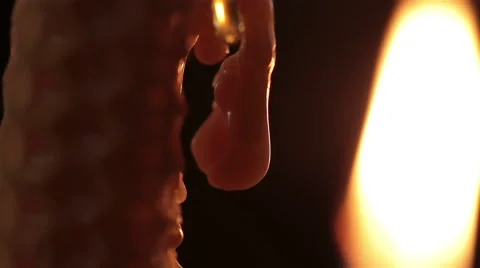 Lit candle flame dripping wax drop macro on black background in church cathedral Stock Footage 48944797