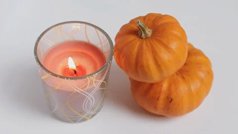 A lit candle flickers next to small orange pumpkins Stock Footage 119012545