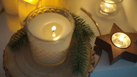 A lit candle placed on a wooden slice, surrounded by pine branches and a Stock Footage 314487810