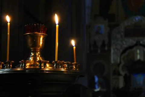 Lit church candles in a gilded candlestick in a temple in the dark. yellow wax Stock Photos