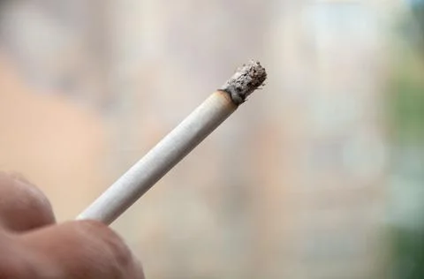 Lit cigarette in hand on a light background Stock Photos