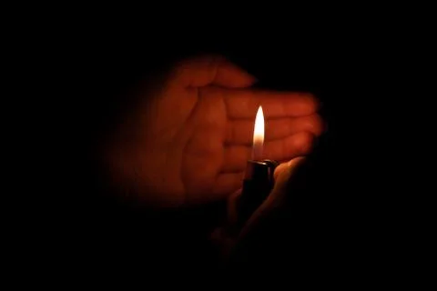 Lit cigarette lighter in one hand in the darkness Stock Photos