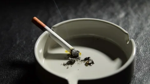 Lit cigarette lying on an empty white ashtray . Stockbeeldmateriaal 125544591