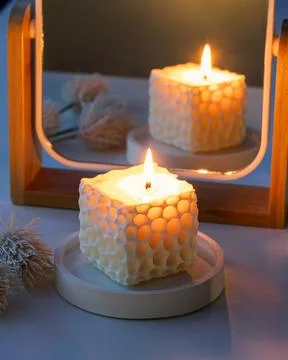 Lit cube handmade soy candle in front of a mirror with dried decorative flowe Stock Photos