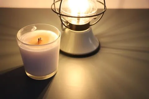 Lit lantern with yellow light and candle next to it, home evening Stock Photos