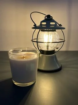 Lit lantern with yellow light and candle next to it, home evening Stock Photos