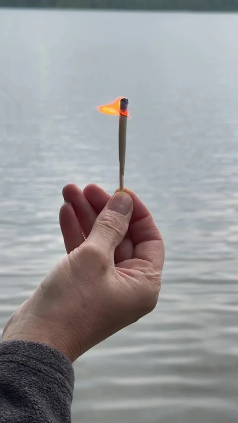Lit match burning steadily above calm lake water. Flame flickering in hand .. Stock Footage 342540900