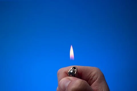Lit small lighter with flame held between fingers by man. Close up studio sho Fotos de archivo