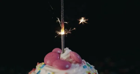 A lit sprinkle candle on top of a cake with pink frosting and sprinkles Stock Footage 317317148