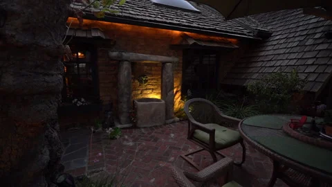 Lit stone water trough and wicker patio set in a brick courtyard Stock Footage 345530308