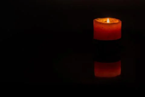 Lit Thick Orange Candle Burning in Dark Studio Setting with Reflection Stock Photos