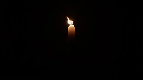 Lit yellow candle on dark background. Close up single candle flame isolated.. Stock Footage 344625400