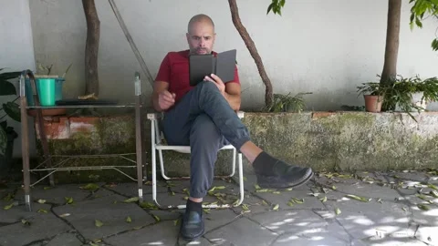 Literature: A man reads an e-reader in the backyard. A person reads an e-book Video stock 320968761