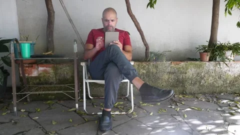 Literature: A person reads an e-reader in the backyard. A man reads an e-book Video stock 321317047