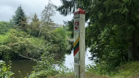 Lithuanian border post stands beside a calm forest river in lush greenery. Stock Footage 273112913