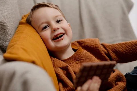 Little adorable boy sitting on the couch at home and eating chocolate bar. Child Stock Photos
