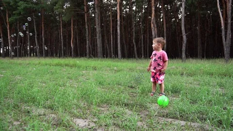Little adorable kid looking at soap bubbles floating around him standing still Stock Footage 104147604