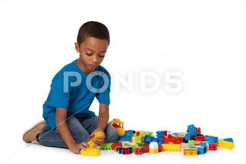 Little african boy playing with lots of colorful plastic blocks indoor. Isolated Stock Photos