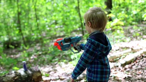 Little amusing happy boy playing with pistol toy shooting at target in sunny Vidéo 156285605