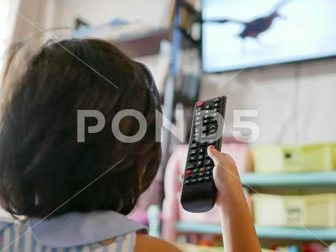 Little Asian baby's hand holding a television remote control, while watching Stock Photos