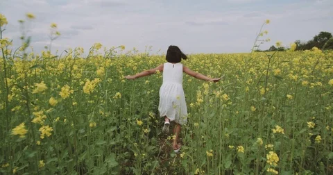 Little Asian girl 8-9 years old running through the field of yellow flowers Stock Footage