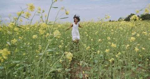 Little Asian girl 8-9 years old running through the field of yellow flowers Stock Footage