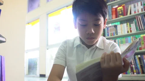 Little Asian student reading book in library . Stock Footage