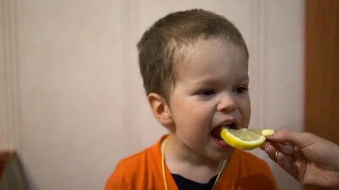 Little baby boy biting a lemon wedge,which holds a woman's hand. Stock Footage