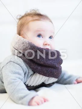 Little baby in a frey knitted sweater and big brown scarf Stock Photos