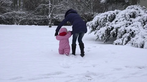Little baby girl learns and her mom teaches to walk on snow in winter day. 4K Stock Footage
