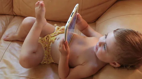 Little baby lying on the couch playing with the tablet. Full HD. 1920x1080 Stock Footage 66428407