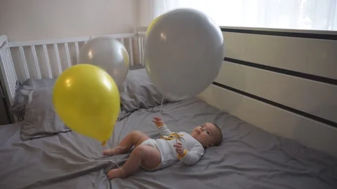 A little baby is playing with ballons on the bed Stock Footage