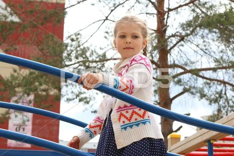 Little beautiful girl plays on children playground in sunny summer day Stock Photos