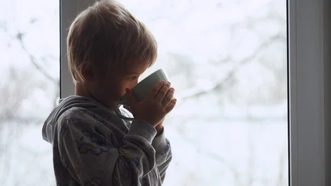 A little blond boy is drinking a hot drink while standing on a window sill  Video stock 100304090