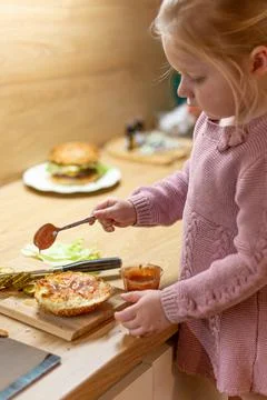 Little blond girl is cooking home made burgers in her kitchen at home Stock Photos