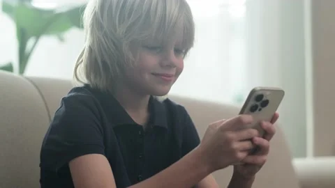 Little blonde boy using looking playing phone and sitting home on couch, holding Stock-Footage 231315710