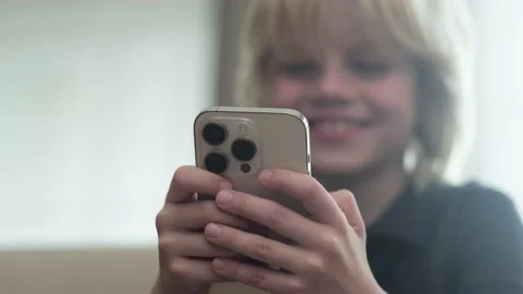 Little blonde boy using looking playing phone and sitting home on couch, holding Video stock 231578366