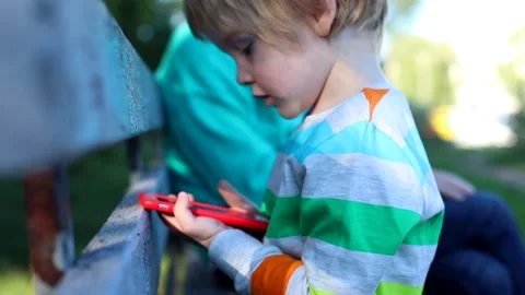 Little blonde boy using smart phone mobile playing games while talking with gran Vidéo 142374032
