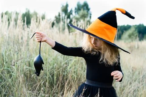 Little blonde girl in a black suit and a witch hat with a black rat in her ha Stock Photos