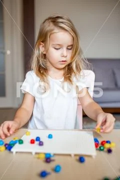 Little blonde girl in a white tshirt playing with plastic multicolor mosaic a Stock Photos