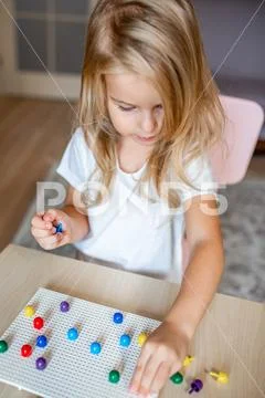 Little blonde girl in a white tshirt playing with plastic multicolor mosaic a Stock Photos